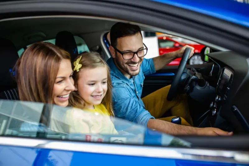 Happy family of three celebrating their new car while sitting inside it